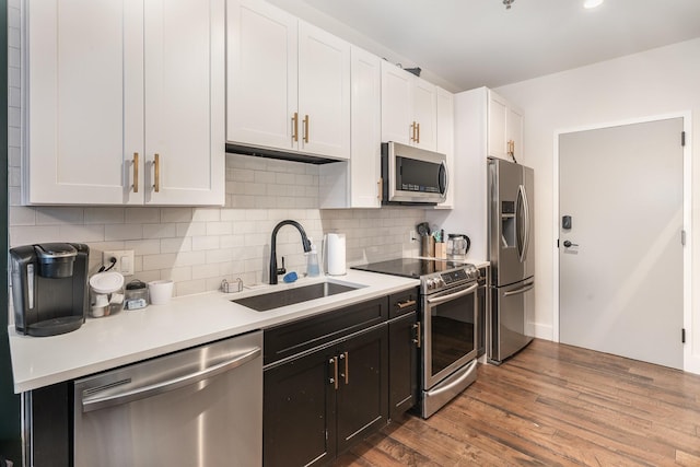 kitchen with decorative backsplash, stainless steel appliances, sink, wood-type flooring, and white cabinetry