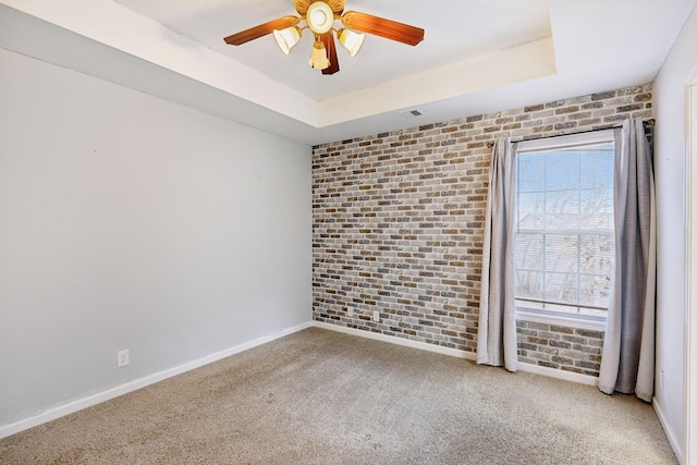 spare room with ceiling fan, brick wall, a tray ceiling, and carpet floors