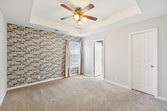 unfurnished bedroom featuring brick wall, light colored carpet, ceiling fan, and a tray ceiling