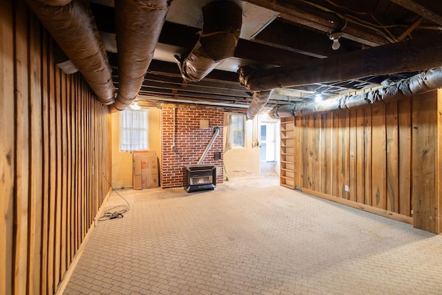 basement featuring a wood stove, wood walls, carpet, and brick wall