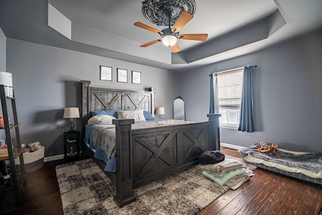 bedroom with a raised ceiling, ceiling fan, and dark wood-type flooring