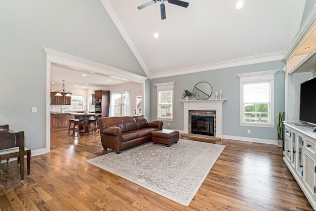 living room featuring a stone fireplace, ceiling fan, a healthy amount of sunlight, and crown molding