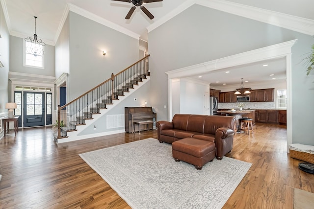 living room featuring hardwood / wood-style floors, a high ceiling, ceiling fan with notable chandelier, and ornamental molding