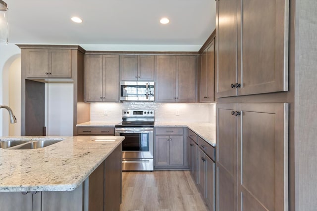 kitchen with appliances with stainless steel finishes, light wood-type flooring, backsplash, light stone counters, and sink