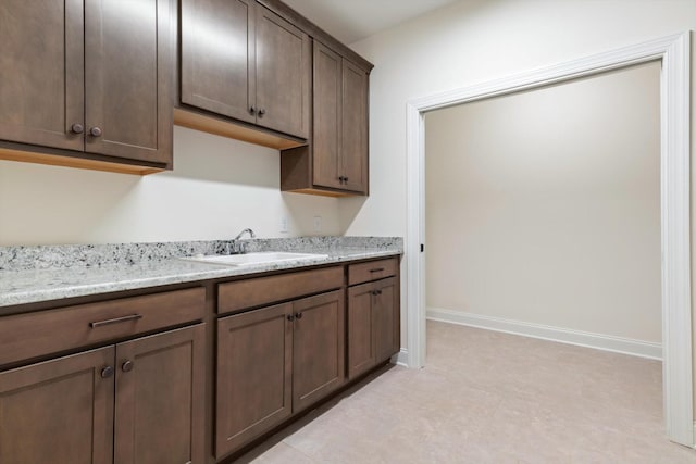 kitchen with dark brown cabinets, light stone counters, and sink