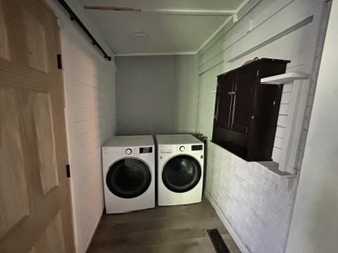 laundry room with a barn door, wood walls, washer and dryer, and wood-type flooring