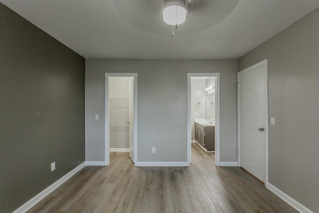 unfurnished bedroom with connected bathroom, a spacious closet, ceiling fan, a closet, and light wood-type flooring