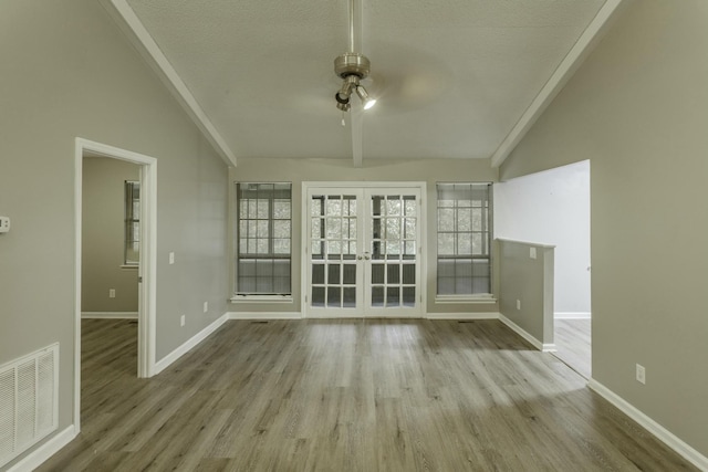 unfurnished room featuring french doors, light wood-type flooring, a textured ceiling, ceiling fan, and beam ceiling