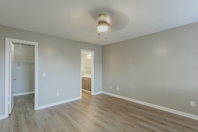 unfurnished bedroom with a walk in closet, ceiling fan, a closet, and light wood-type flooring