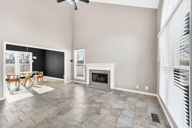 unfurnished living room with a fireplace, a towering ceiling, and ceiling fan with notable chandelier