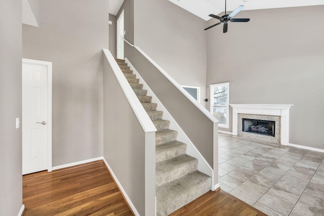 stairs with ceiling fan, a fireplace, hardwood / wood-style floors, and a high ceiling