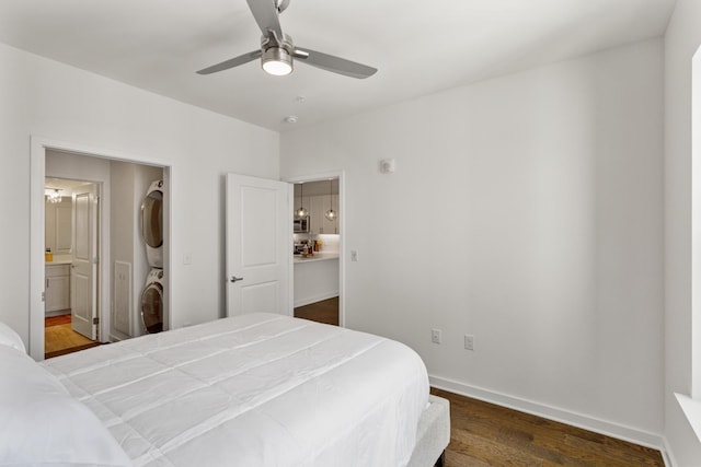 bedroom featuring dark hardwood / wood-style floors, ceiling fan, ensuite bathroom, and stacked washer and clothes dryer