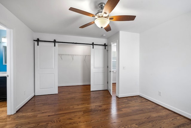 unfurnished bedroom featuring ceiling fan, a barn door, dark hardwood / wood-style flooring, and a closet