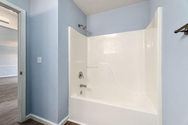 bathroom with a textured ceiling,  shower combination, and hardwood / wood-style flooring