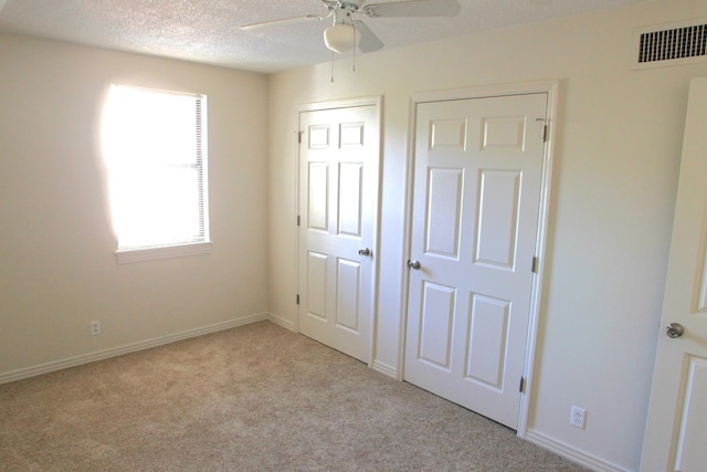 unfurnished bedroom featuring a textured ceiling, light colored carpet, and ceiling fan