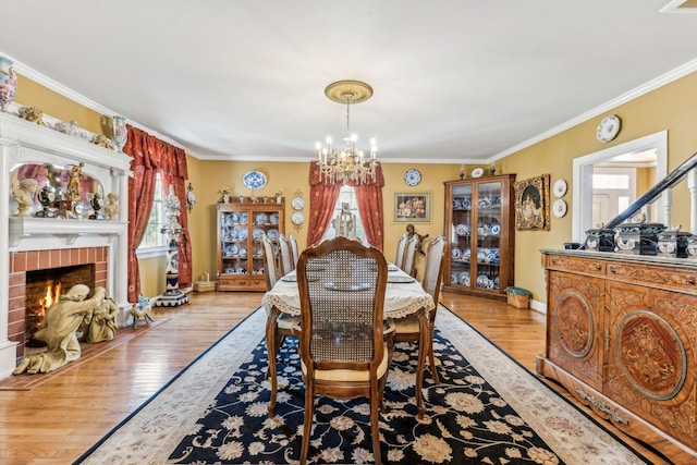 dining room with a notable chandelier, light hardwood / wood-style floors, ornamental molding, and a brick fireplace