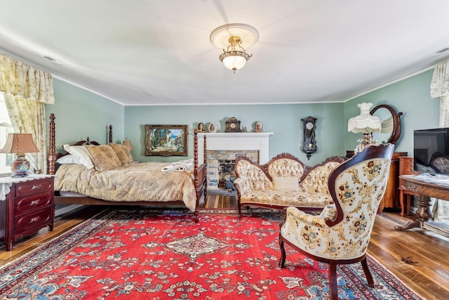 bedroom featuring a fireplace, wood-type flooring, and crown molding