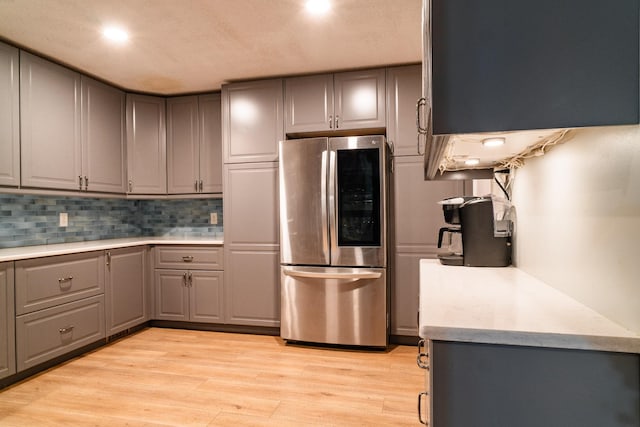 kitchen with gray cabinetry, backsplash, stainless steel refrigerator, and light hardwood / wood-style flooring