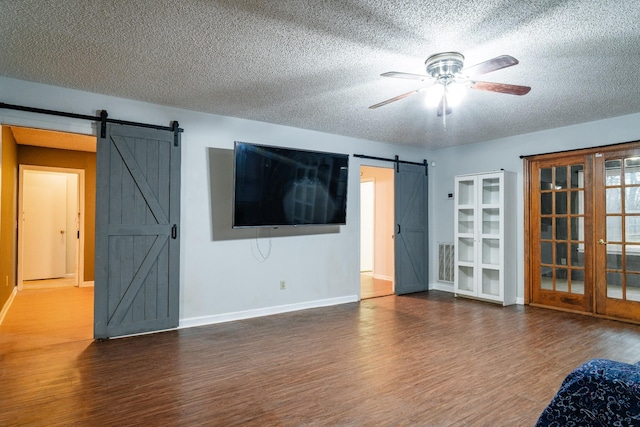 spare room featuring french doors, a barn door, ceiling fan, and dark wood-type flooring