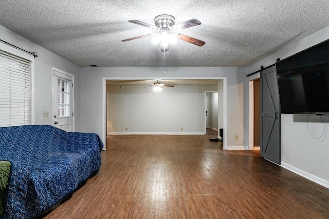 living room featuring ceiling fan, a barn door, dark hardwood / wood-style flooring, and a textured ceiling