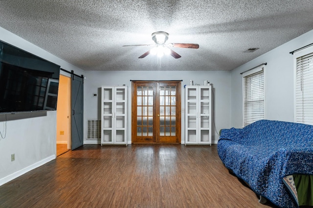 living area featuring ceiling fan, french doors, a barn door, dark hardwood / wood-style flooring, and a textured ceiling