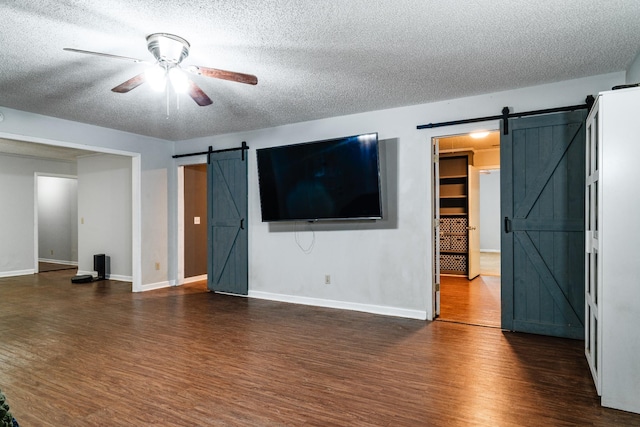 unfurnished living room featuring a textured ceiling, ceiling fan, a barn door, and dark hardwood / wood-style floors