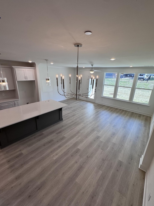 unfurnished living room featuring an inviting chandelier, wood finished floors, and baseboards