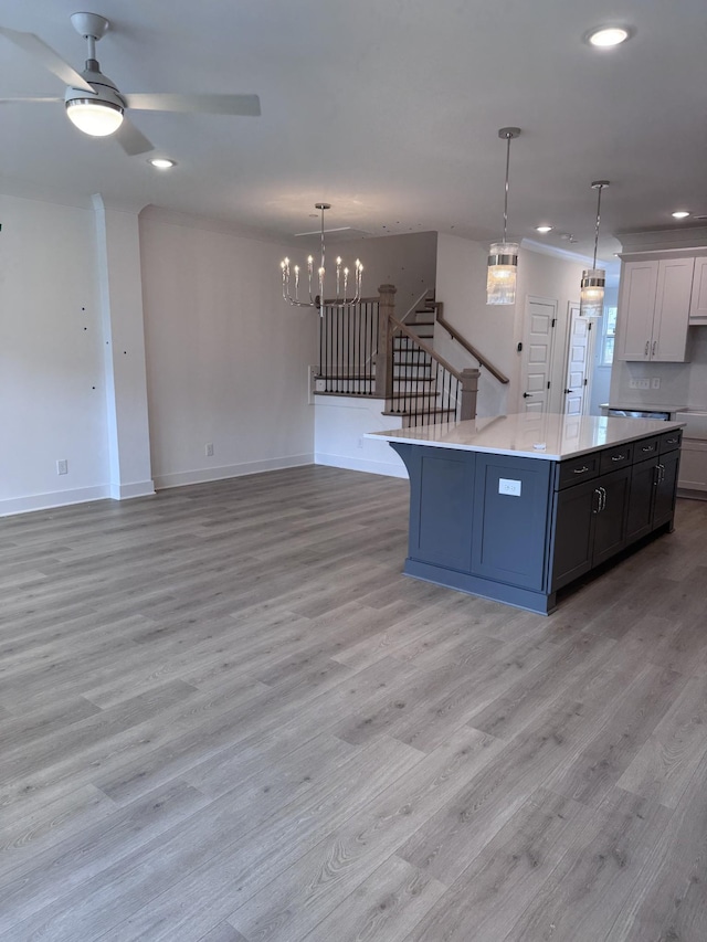 kitchen featuring pendant lighting, ceiling fan with notable chandelier, a kitchen island, light wood finished floors, and light countertops