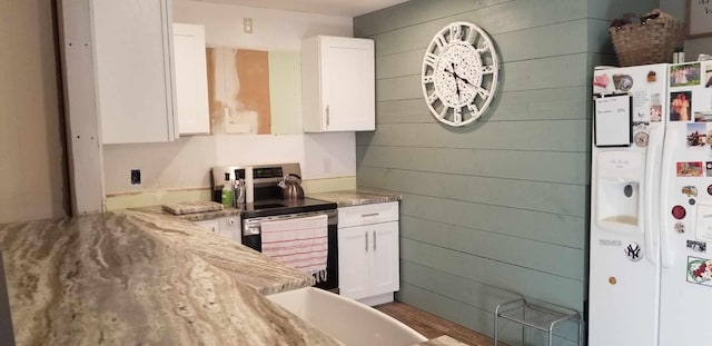 kitchen featuring white cabinets, stainless steel range with electric stovetop, white fridge with ice dispenser, and wood walls