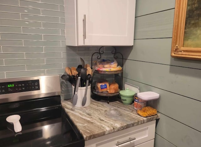 kitchen featuring light stone countertops, white cabinetry, stainless steel stove, and tasteful backsplash