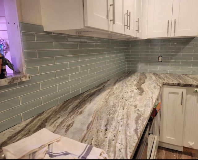 interior details featuring decorative backsplash, white cabinetry, and light stone countertops