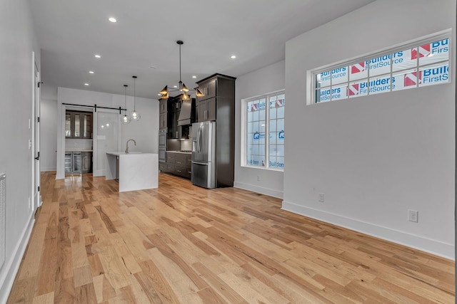 unfurnished living room featuring baseboards, a barn door, recessed lighting, and light wood-style floors