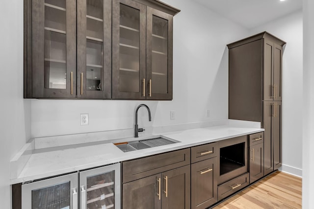 kitchen featuring dark brown cabinetry, beverage cooler, light wood finished floors, glass insert cabinets, and a sink