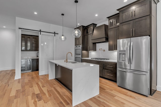 kitchen featuring a barn door, appliances with stainless steel finishes, light countertops, premium range hood, and a sink