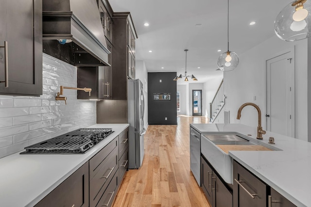 kitchen with black gas stovetop, light wood-style flooring, a sink, custom exhaust hood, and freestanding refrigerator