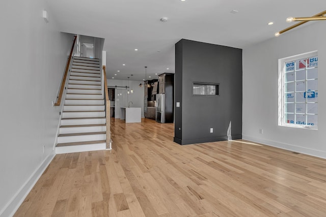 unfurnished living room with light wood-style flooring, stairs, baseboards, and recessed lighting