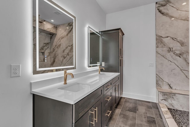 full bath with double vanity, a marble finish shower, baseboards, and a sink