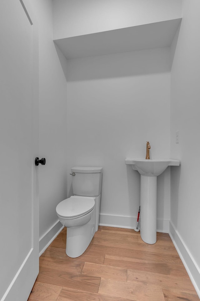 half bathroom with toilet, baseboards, and wood finished floors