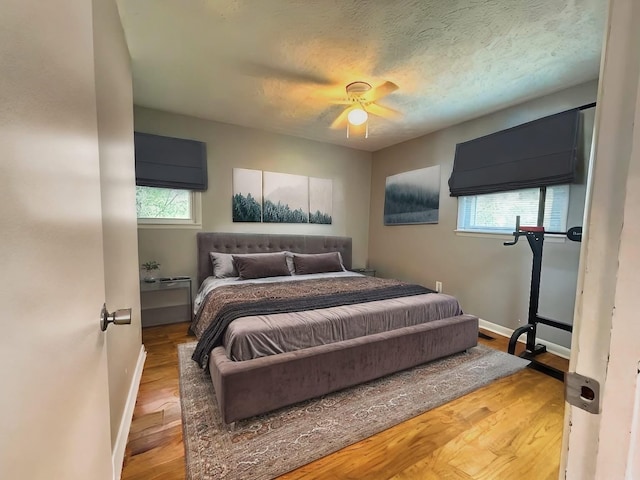 bedroom with ceiling fan, wood-type flooring, a textured ceiling, and multiple windows