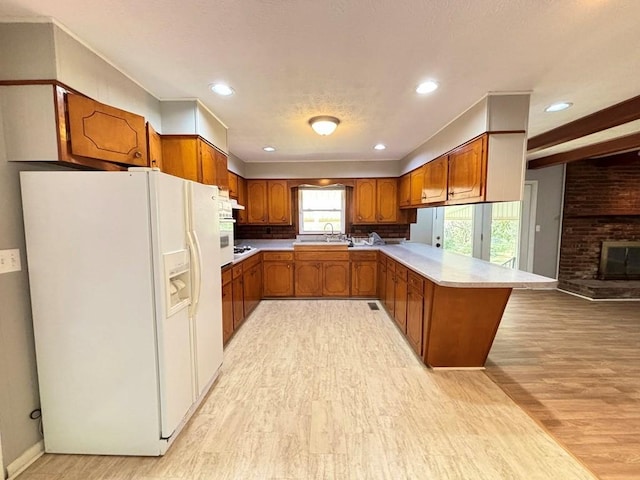 kitchen featuring sink, light hardwood / wood-style flooring, a brick fireplace, white fridge with ice dispenser, and kitchen peninsula