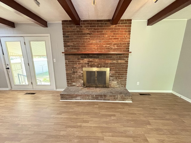 unfurnished living room featuring beamed ceiling, a fireplace, light wood-type flooring, and a textured ceiling