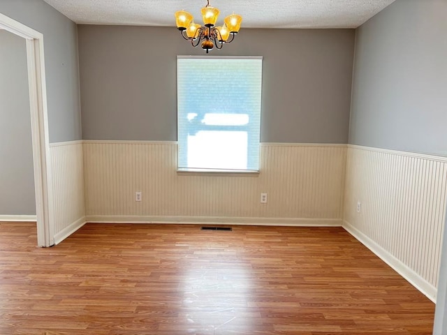 spare room with hardwood / wood-style flooring, a textured ceiling, and an inviting chandelier