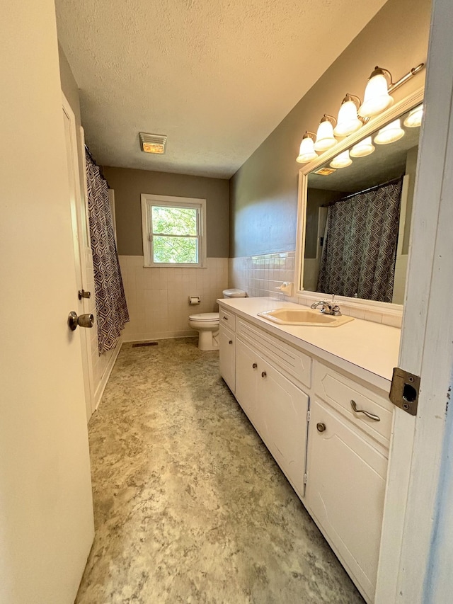 bathroom with vanity, a textured ceiling, toilet, and tile walls