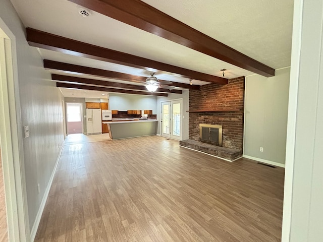 unfurnished living room featuring beamed ceiling, ceiling fan, a healthy amount of sunlight, and light wood-type flooring