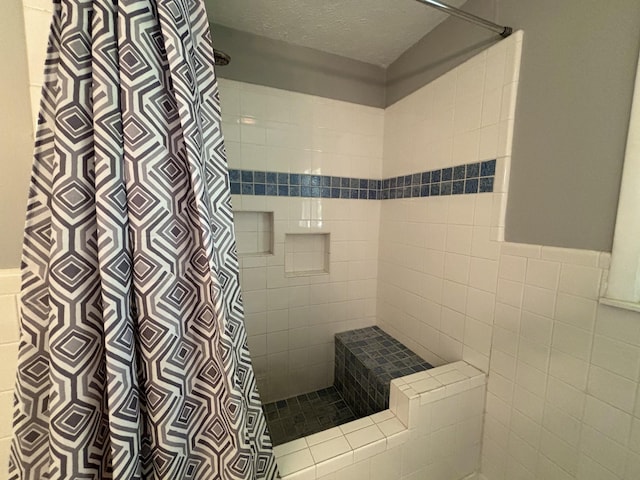 bathroom featuring a textured ceiling, tiled shower, and tile walls