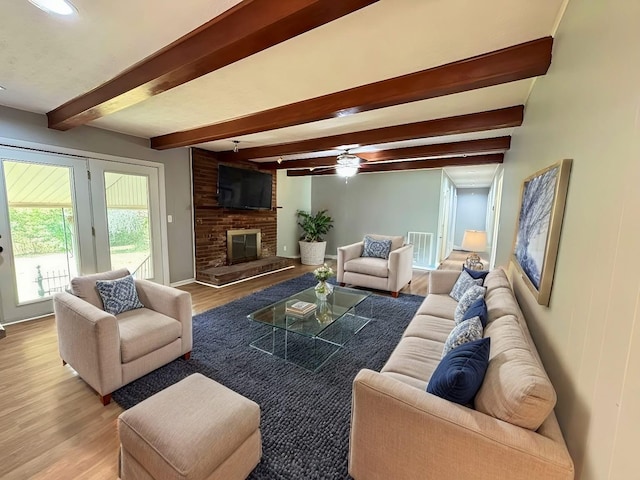 living room with beamed ceiling, light hardwood / wood-style flooring, a brick fireplace, and ceiling fan