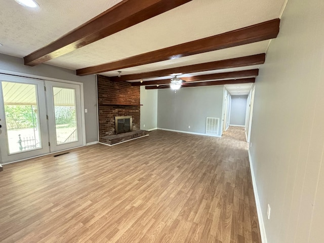 unfurnished living room with a brick fireplace, ceiling fan, light wood-type flooring, a textured ceiling, and beamed ceiling