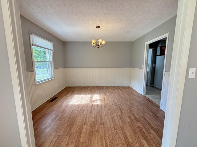 empty room featuring a textured ceiling, hardwood / wood-style flooring, and a notable chandelier