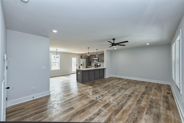 unfurnished living room featuring ceiling fan with notable chandelier and dark wood-type flooring