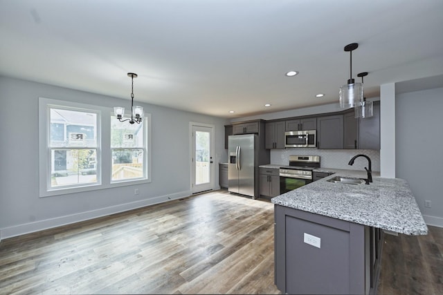 kitchen featuring light stone countertops, sink, stainless steel appliances, an inviting chandelier, and decorative light fixtures